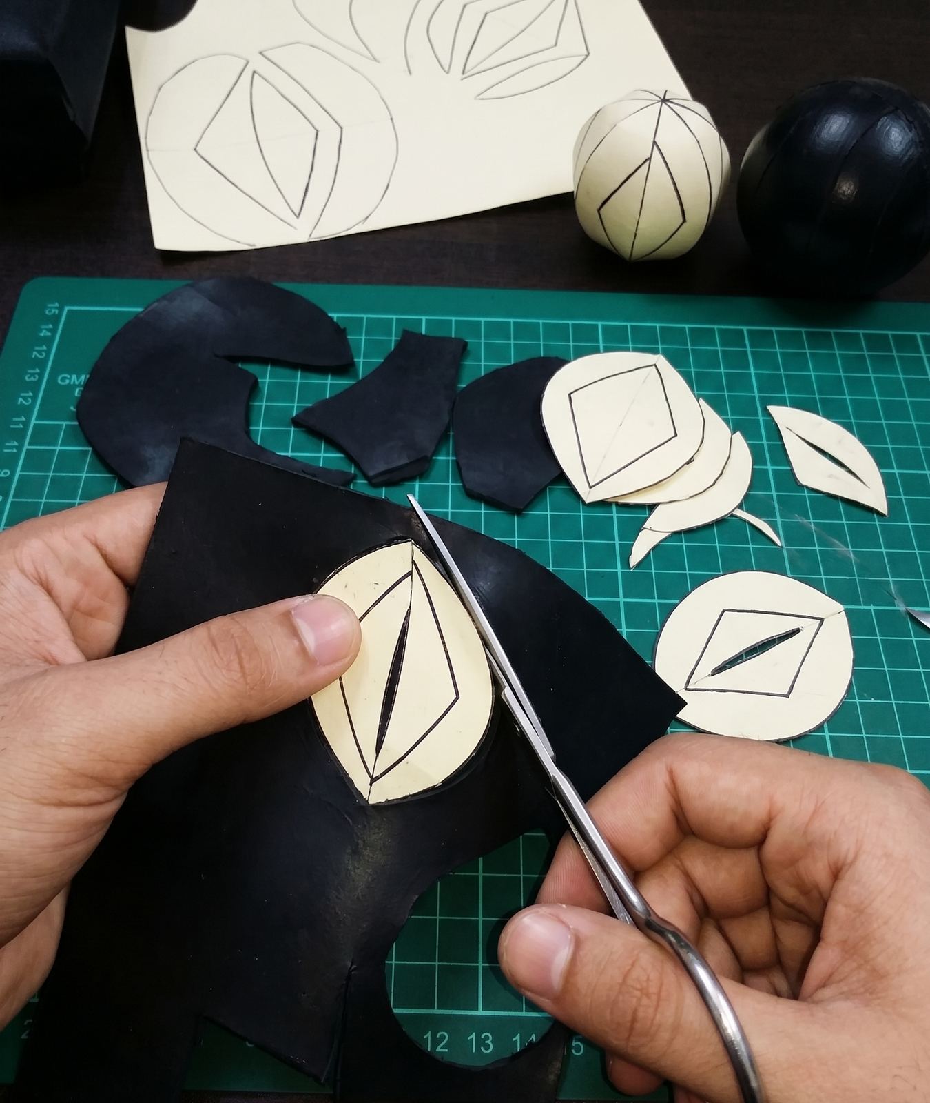 Cutting ball panels from the paper pattern, with a paper prototype ball and a finished black ball on the workbench
