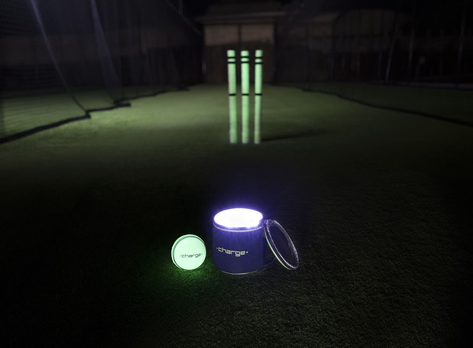 A glowing Chargeball and Chargebag beside glowing cricket stumps on an indoor pitch