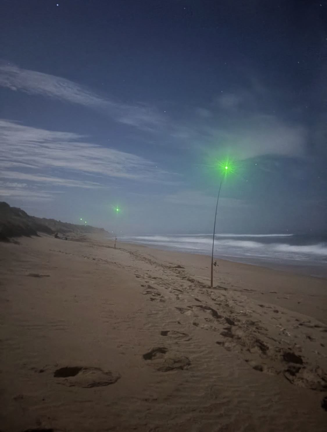 Two rods planted in the sand at night, their Rod Tip clips glowing green against a dark sky